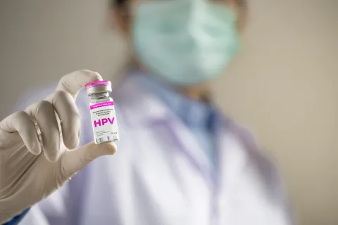 Photographie d'une professionnelle de santé masquée et gantée tenant un flacon de vaccin étiqueté HPV
